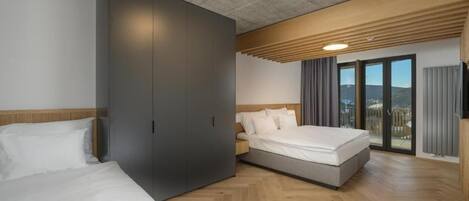 A modern hotel room with two beds, a large wardrobe, and a balcony with a view.