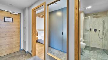 A modern bathroom with a glass shower, a wooden door, and a mirror.