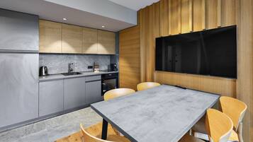 Une cuisine moderne avec des meubles gris, un four encastré et une grande table à manger entourée de chaises en bois.
