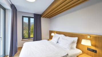 Una habitación de hotel moderna con una cama grande, cabecera de madera, dos lámparas de noche y un ventanal con cortinas.