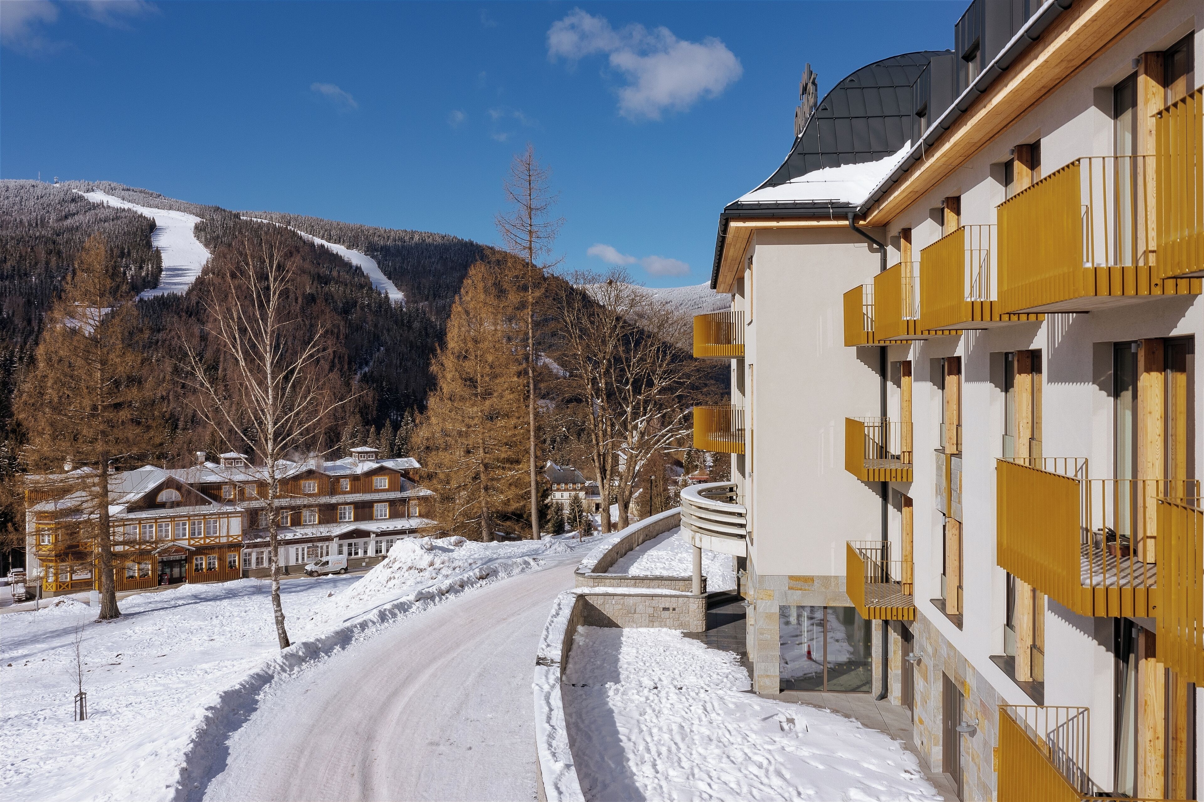 A snow-covered road leading to a building with balconies and a mountain backdrop.