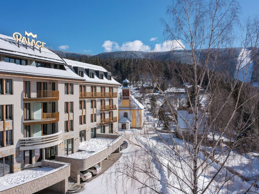 Un hotel llamado "Palace", con un diseño moderno, múltiples balcones y vistas a un paisaje nevado con montañas al fondo.