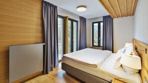 Ein modernes Hotelzimmer mit einem großen Bett, Holzboden und großen Fenstern mit Vorhängen.