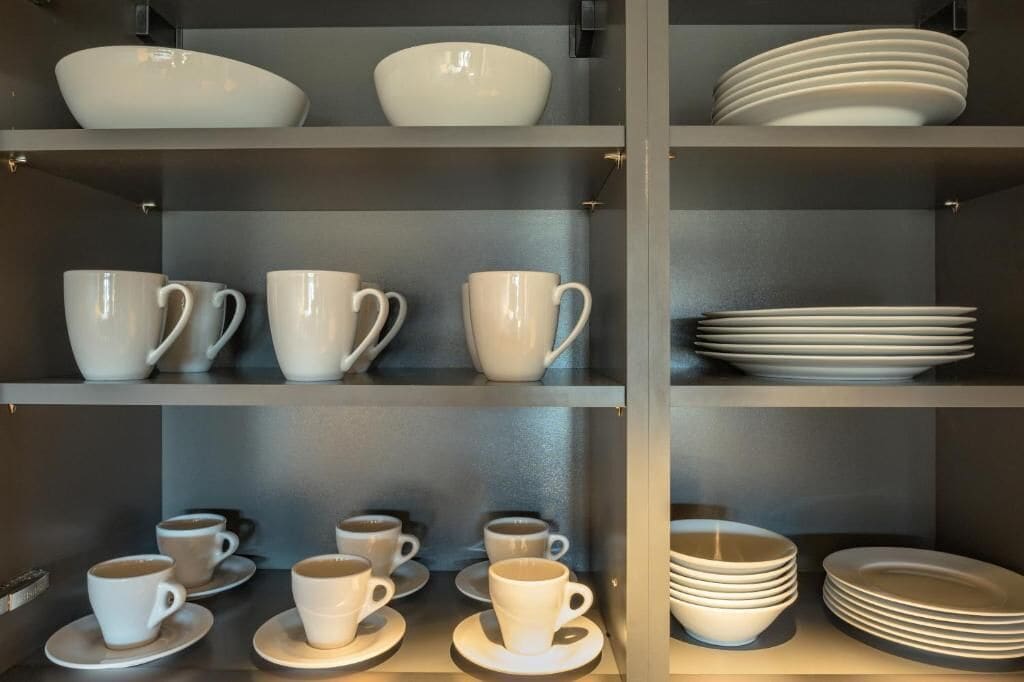 Un ensemble d’étagères avec des tasses et des soucoupes blanches, ainsi que des assiettes empilées.