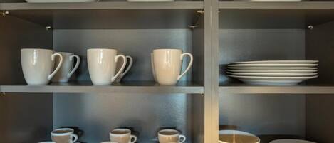 Unos estantes con tazas y platillos blancos, y platos apilados.