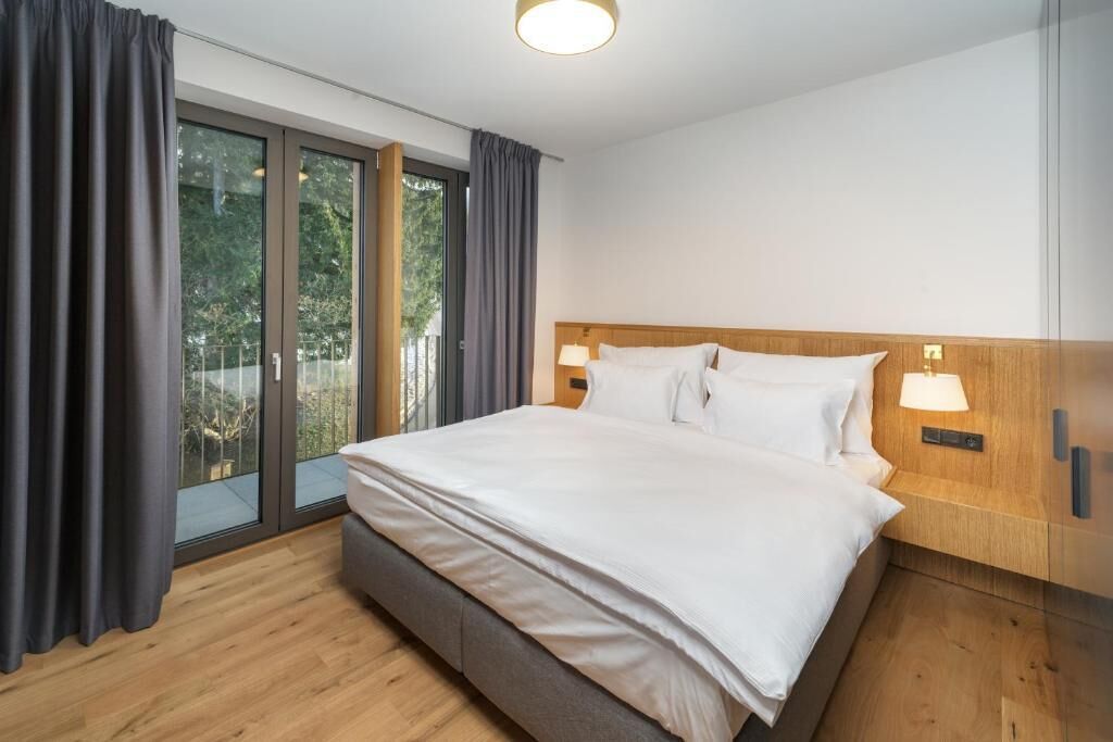 Ein modernes Hotelzimmer mit einem großen Bett, einem Holzkopfbrett und einer Schiebetür zu einem Balkon.