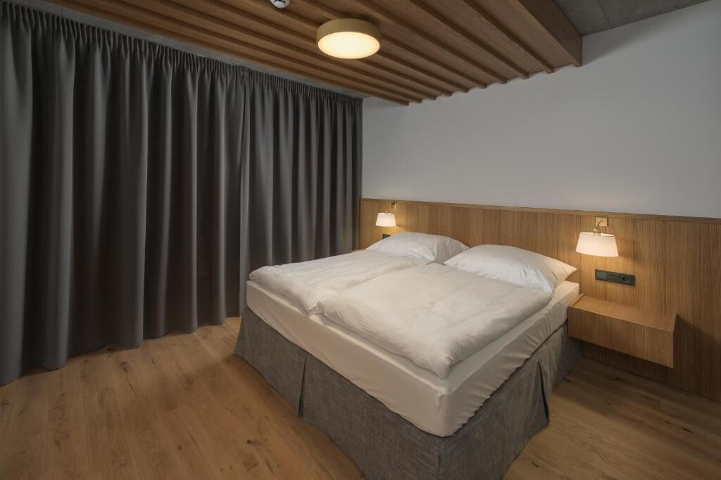 Un dormitorio con cabecera de madera, dos lámparas de noche, cama con ropa blanca y suelo de madera.