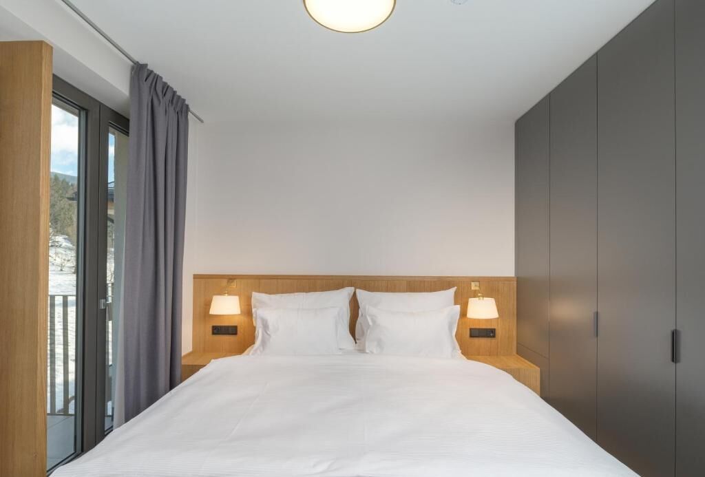 Et moderne hotelværelse med en stor seng, to sengeborde med lamper, en træhovedgærde og udsigt gennem en glasdør.