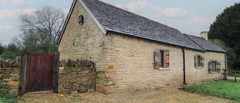 A stone building with a sloped roof, a wooden door, and a small window with shutters.