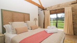 Quarto com uma cama grande, cabeceira, abajur e vista do exterior pela janela.