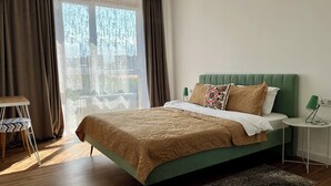 Une chambre à coucher moderne avec un lit recouvert d’un tissu vert, un plaid à motifs et une petite table de chevet avec une lampe.