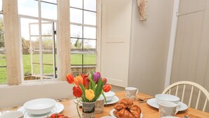 A dining table set with plates, cups, and a bowl of strawberries, with a window view of a garden. - The Smithy (Moreton-in-Marsh)