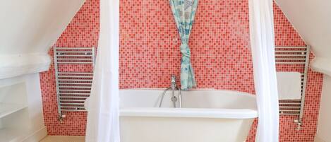 A bathroom with a freestanding bathtub, a shower curtain with a fish pattern, and red mosaic tiles on the walls.