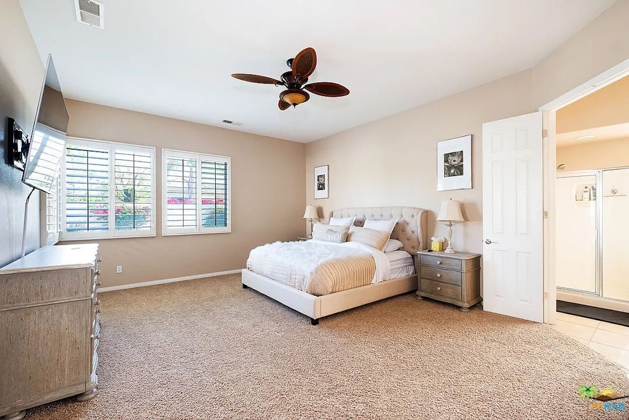 A bedroom with a bed, a dresser, a ceiling fan, and a door leading to another room.