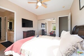 A bedroom with a bed, a television, a ceiling fan, and a bathroom visible through an open door. - Gated Rancho Mirage Oasis w/ Pool & Spa (Rancho Mirage)