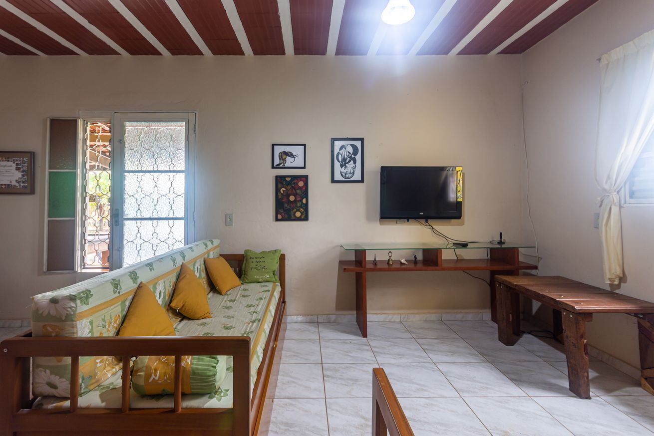 Un salon avec un canapé, une table en verre, un banc en bois et un téléviseur fixé au mur.