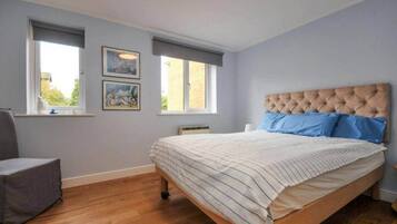 Une chambre à coucher avec un lit, deux fenêtres, une chaise et des œuvres d’art accrochées au mur.