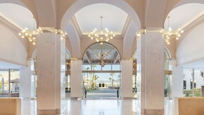 Um hall amplo com tetos altos, colunas de mármore e um lustre central.