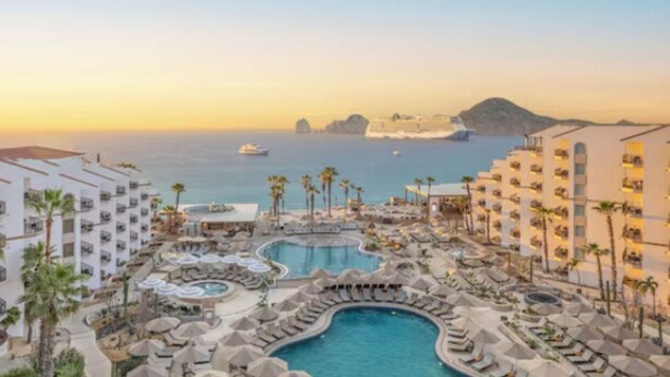 Um resort com várias piscinas, palmeiras e vista para o mar e ilhas distantes.