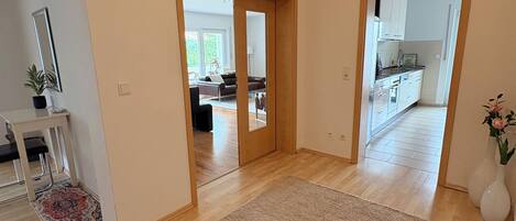 Un pasillo espacioso con suelo de madera, un tapete color beige y un espejo a la izquierda.