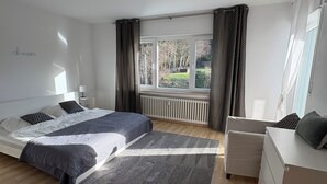 Ein modernes Schlafzimmer mit einem großen Bett, einem Nachttisch, einer Kommode und einem Fenster mit Vorhängen.