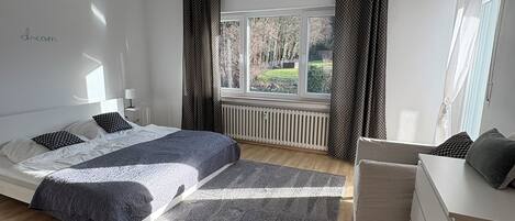 A modern bedroom with a large bed, a bedside table, a dresser, and a window with curtains.