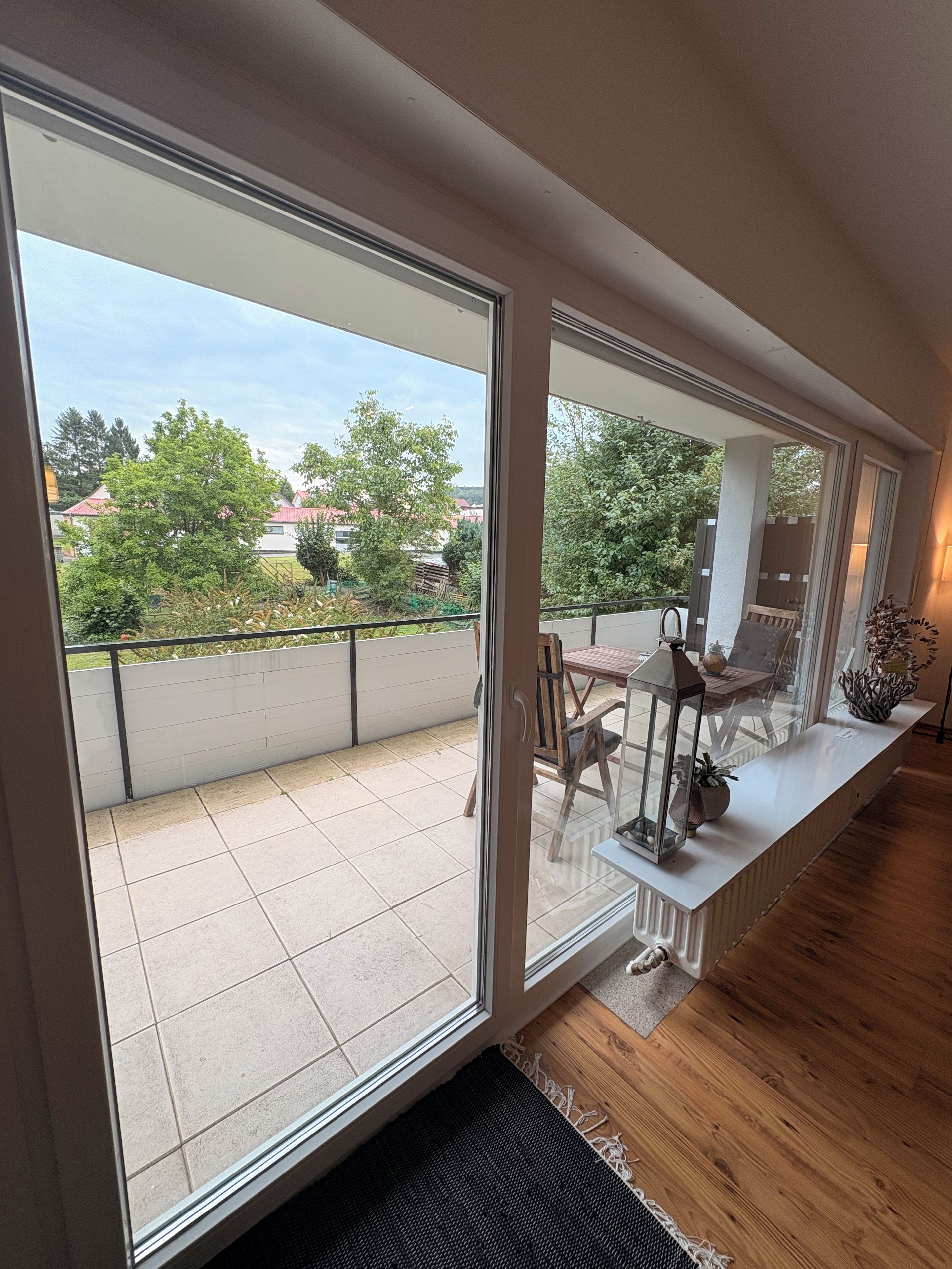 Ein Balkon mit Blick auf einen Garten und Gebäude, ein Holztisch mit Stühlen und einem Geländer.
