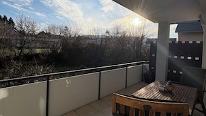 Ein Balkon mit Holztisch und -stühlen, Blick auf die Landschaft und ein Gebäude im Hintergrund.