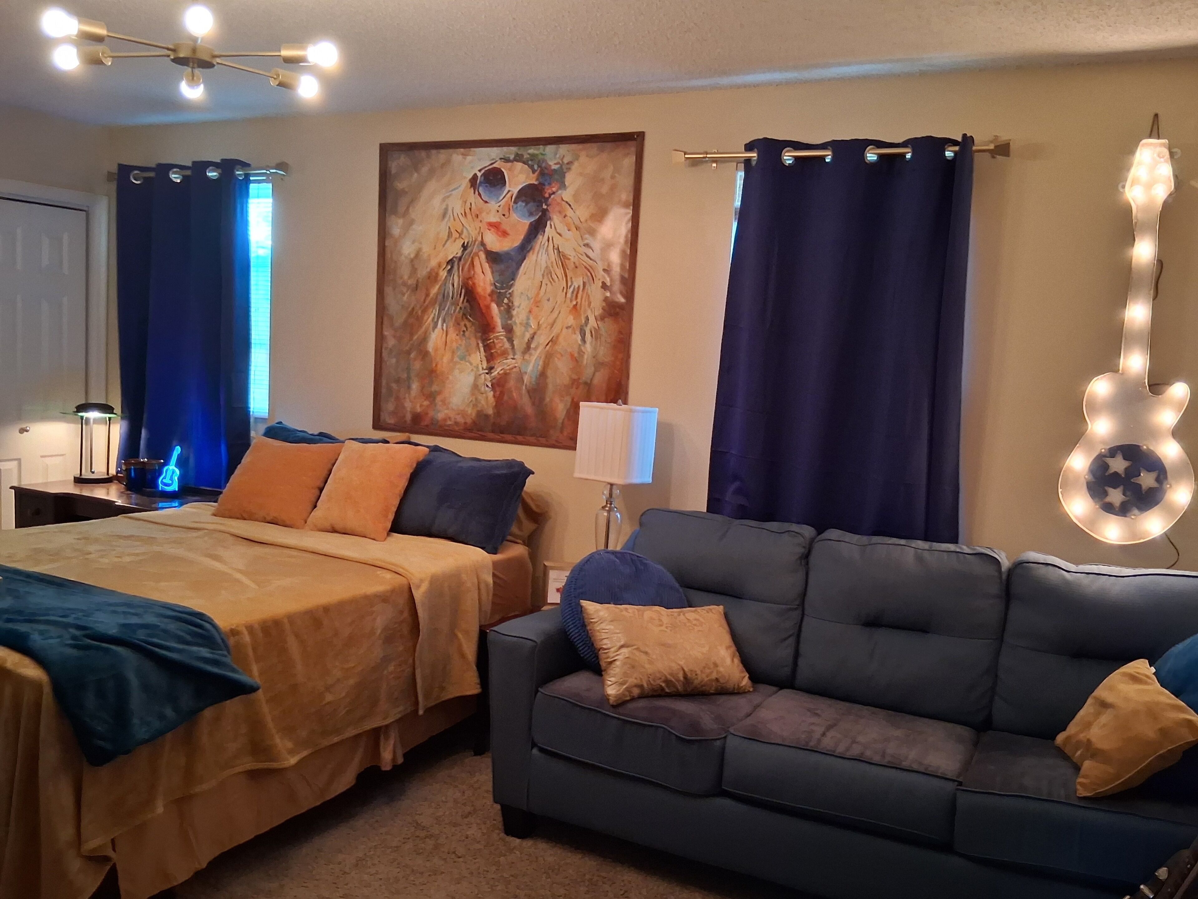 Ein Schlafzimmer mit zwei Betten, einem Sofa, einer lampenartigen Leuchte in Gitarrenform und einem Bild an der Wand.