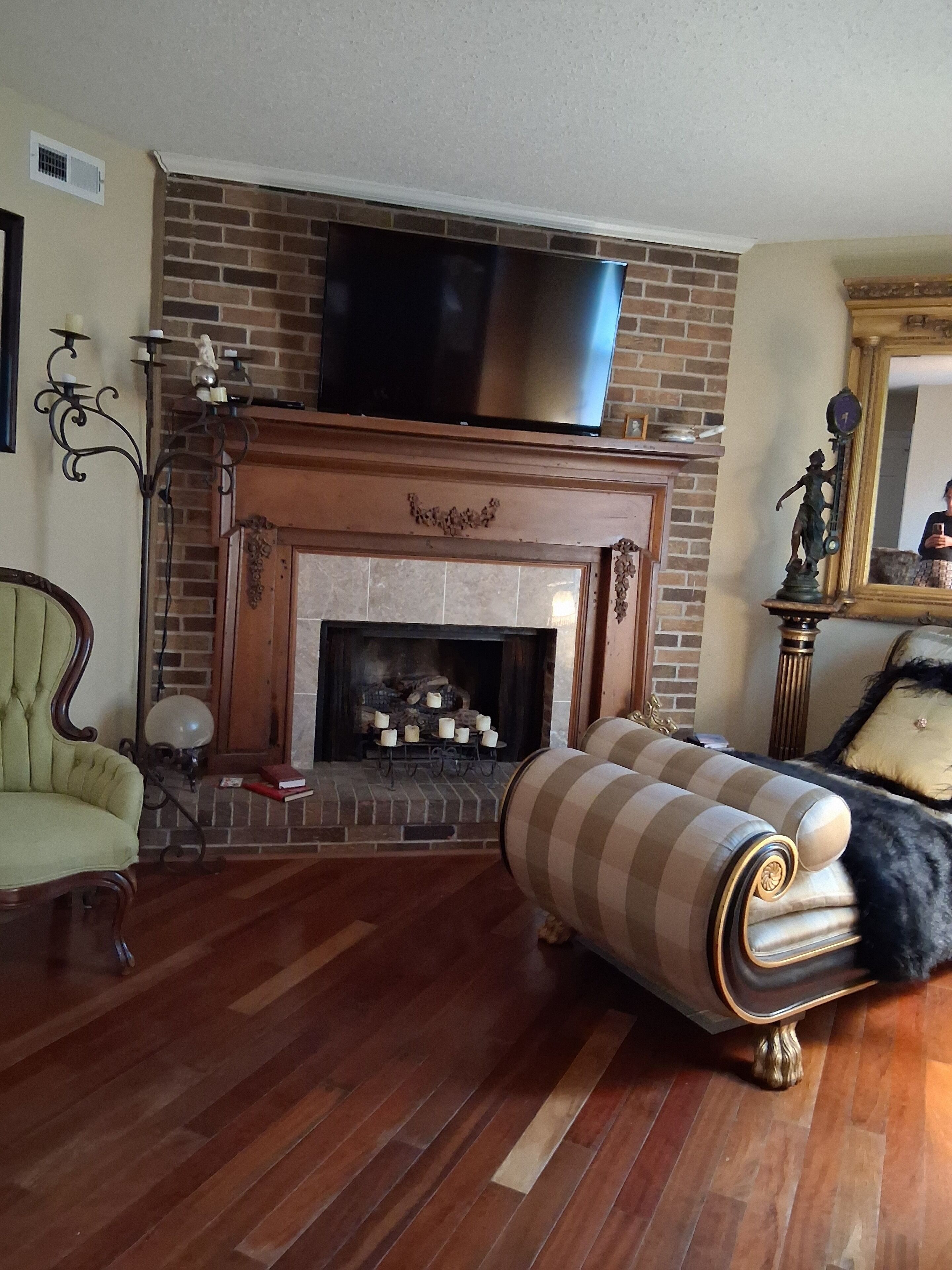 Un salon avec une cheminée en briques, un téléviseur à écran plat fixé au-dessus, un fauteuil à rayures et un plancher en bois.