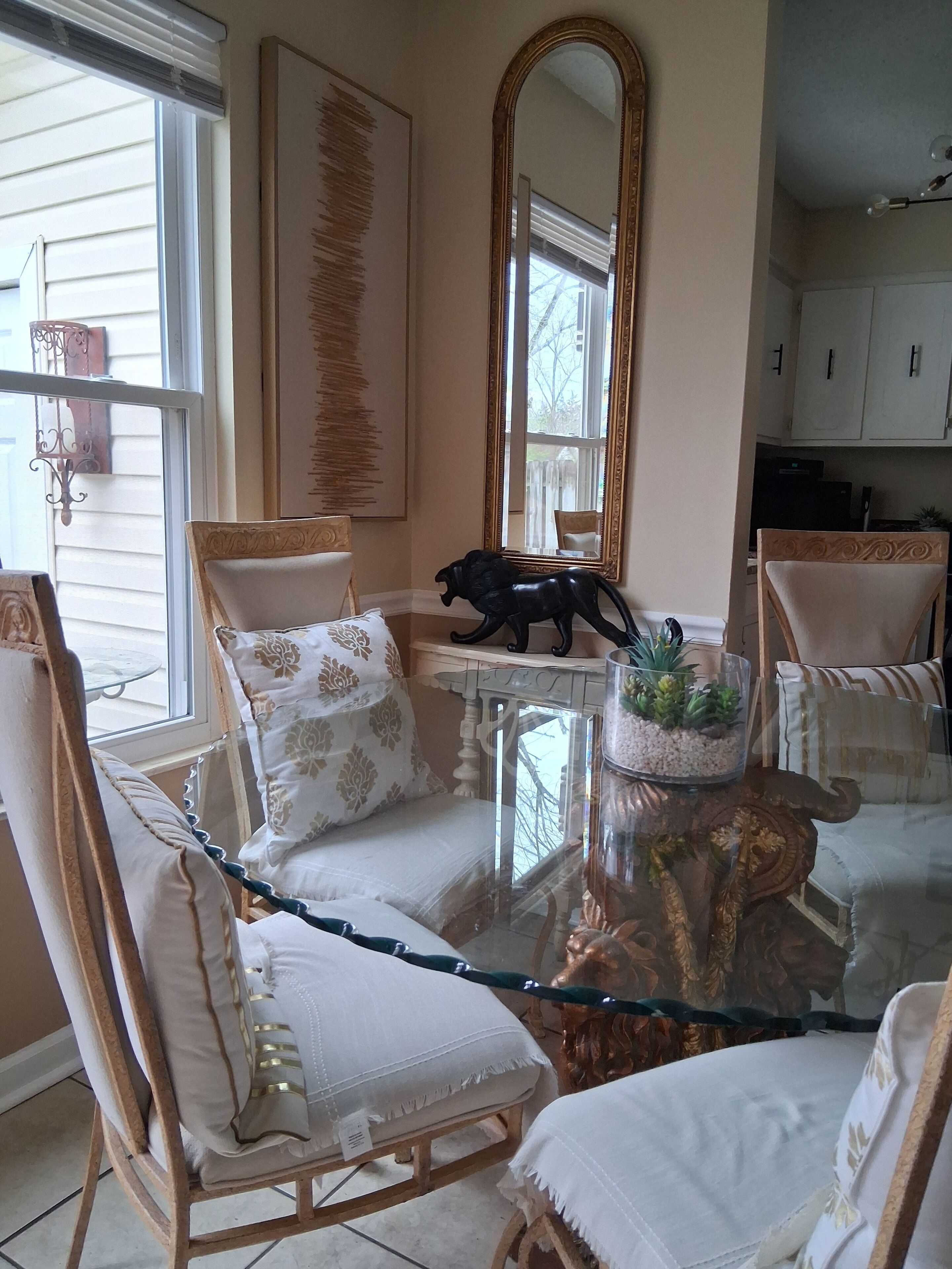 A room with a glass coffee table, white cushioned chairs, a large mirror, and a decorative plant.