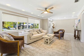 A bright living room with neutral seating, a coffee table, and views of palm trees. - Newly appointed home w/Pool & Gulf Access (Sarasota)