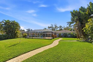 A curved paver path crosses the large green lawn toward a screened pool enclosure. - Newly appointed home w/Pool & Gulf Access (Sarasota)