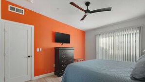 A bedroom with an orange wall, a ceiling fan, a TV, a dresser, and a bed with a blue bedspread. - Cozy One Bedroom Oldtown EV Charger Shared Space (Scottsdale)