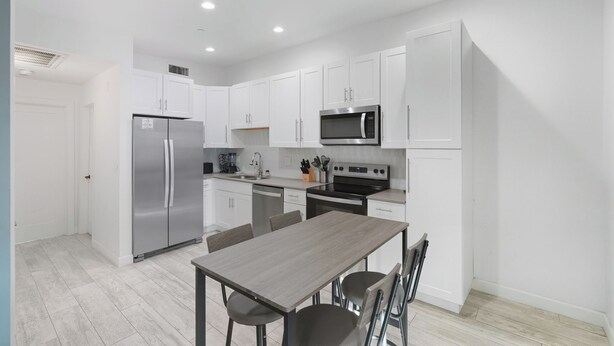 A modern kitchen with white cabinets, stainless steel appliances, and a wooden dining table. - Cozy One Bedroom Oldtown EV Charger Shared Space (Scottsdale)