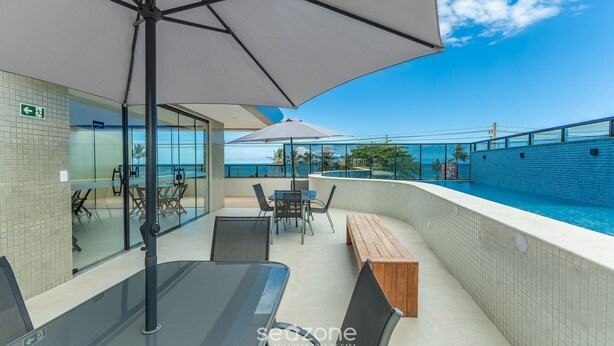 A rooftop terrace with a pool, outdoor seating, and a glass wall offering a view of the ocean. - Apto Vista Mar Lateral em Frente a Praia BDT0608 (Ilhéus)