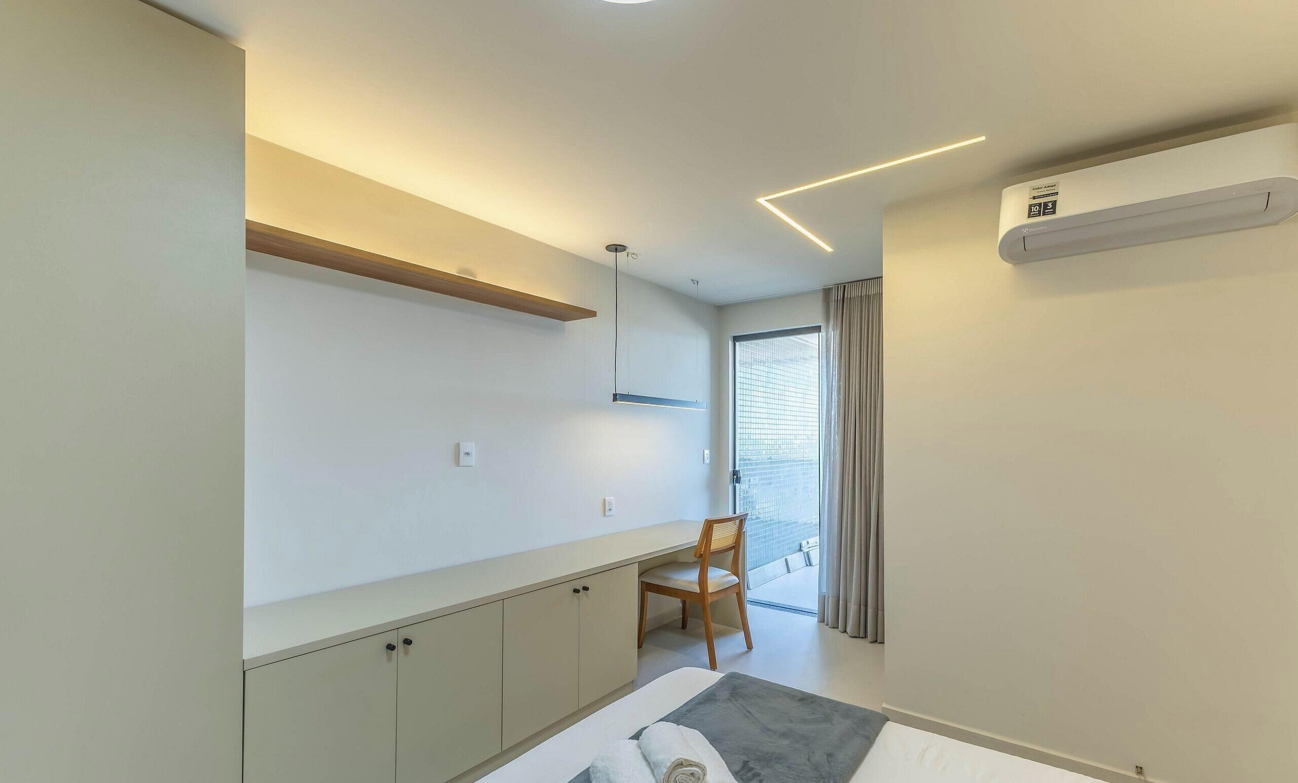 A modern bedroom with a bed, a desk, a chair, and a large window with curtains.