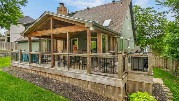 Ein Haus mit überdachter Terrasse, umzäuntem Deck und Schornstein.