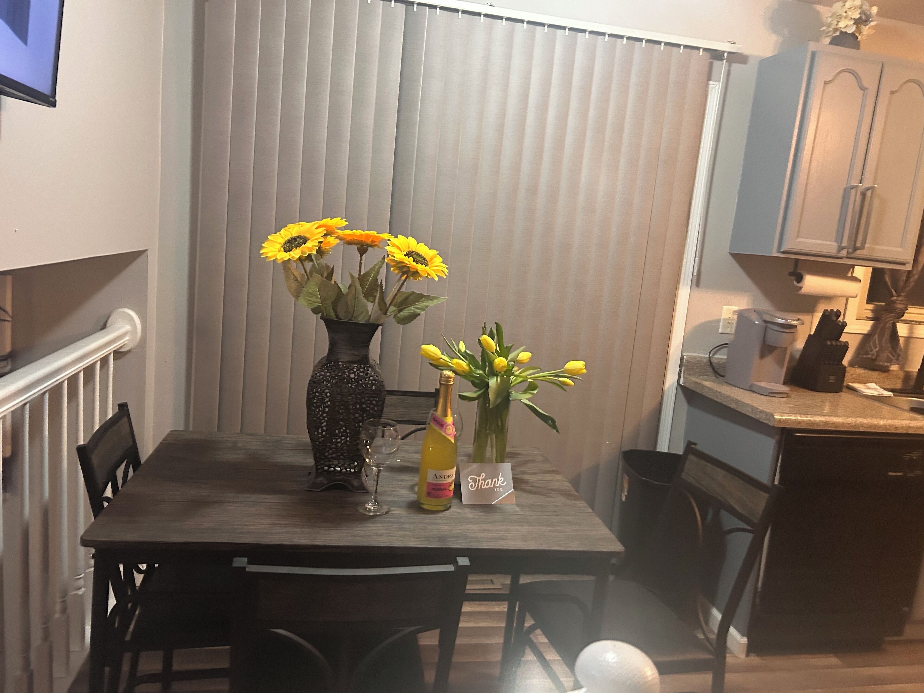 A dining table with two vases, one with sunflowers and one with tulips, and a bottle of wine.