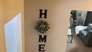 Un saló amb un cartell que diu 'HOME', una taula petita amb una làmpada i un sofà gris.