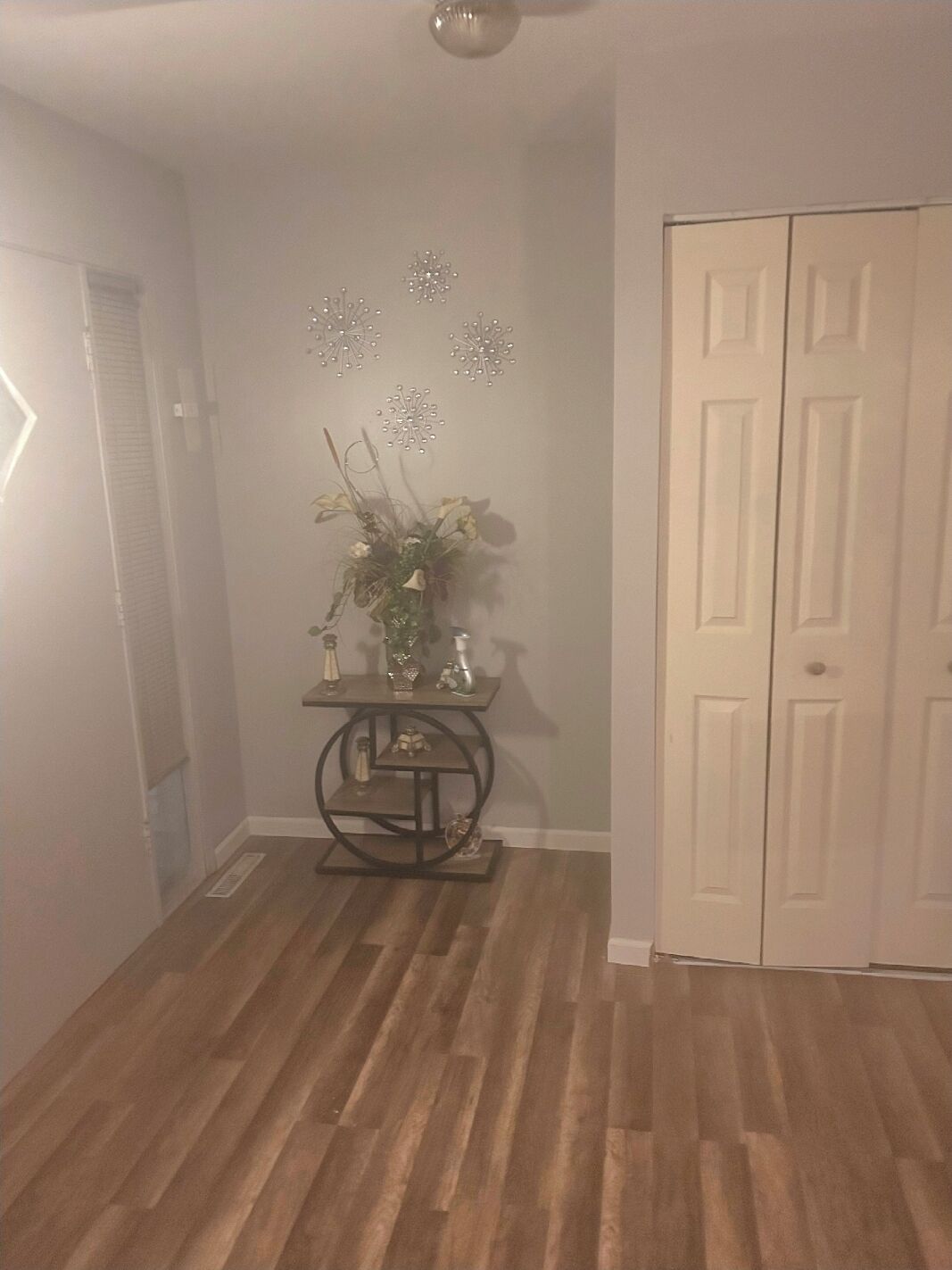 A hallway with a wooden floor, a white door, and a small table with decorative items.