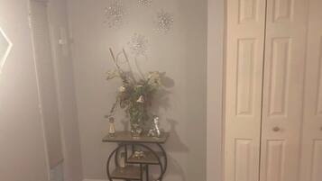A hallway with a wooden floor, a white door, and a small table with decorative items.