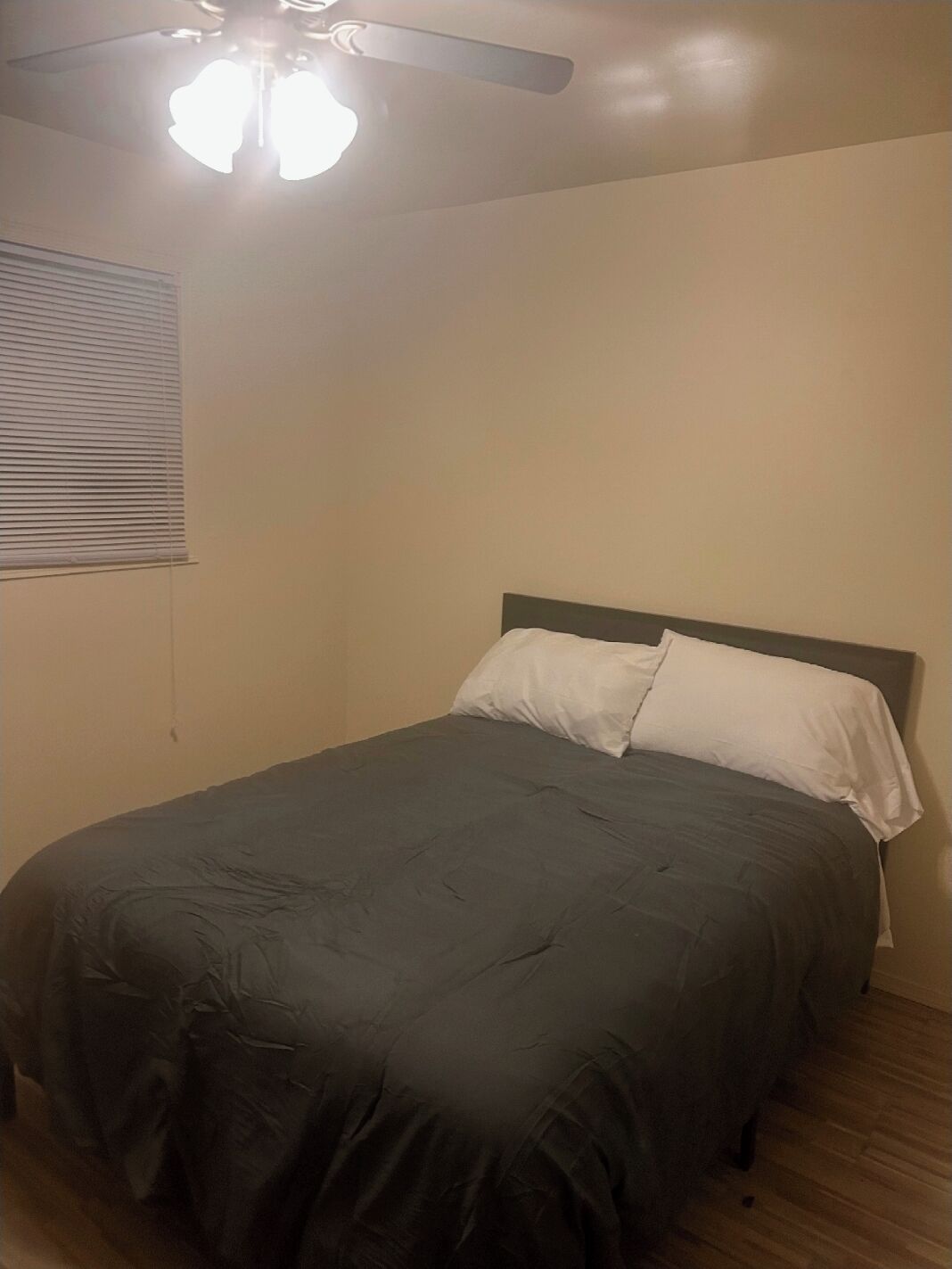Ein Schlafzimmer mit einem Einzelbett, einem Deckenventilator und einem Fenster mit Jalousien.