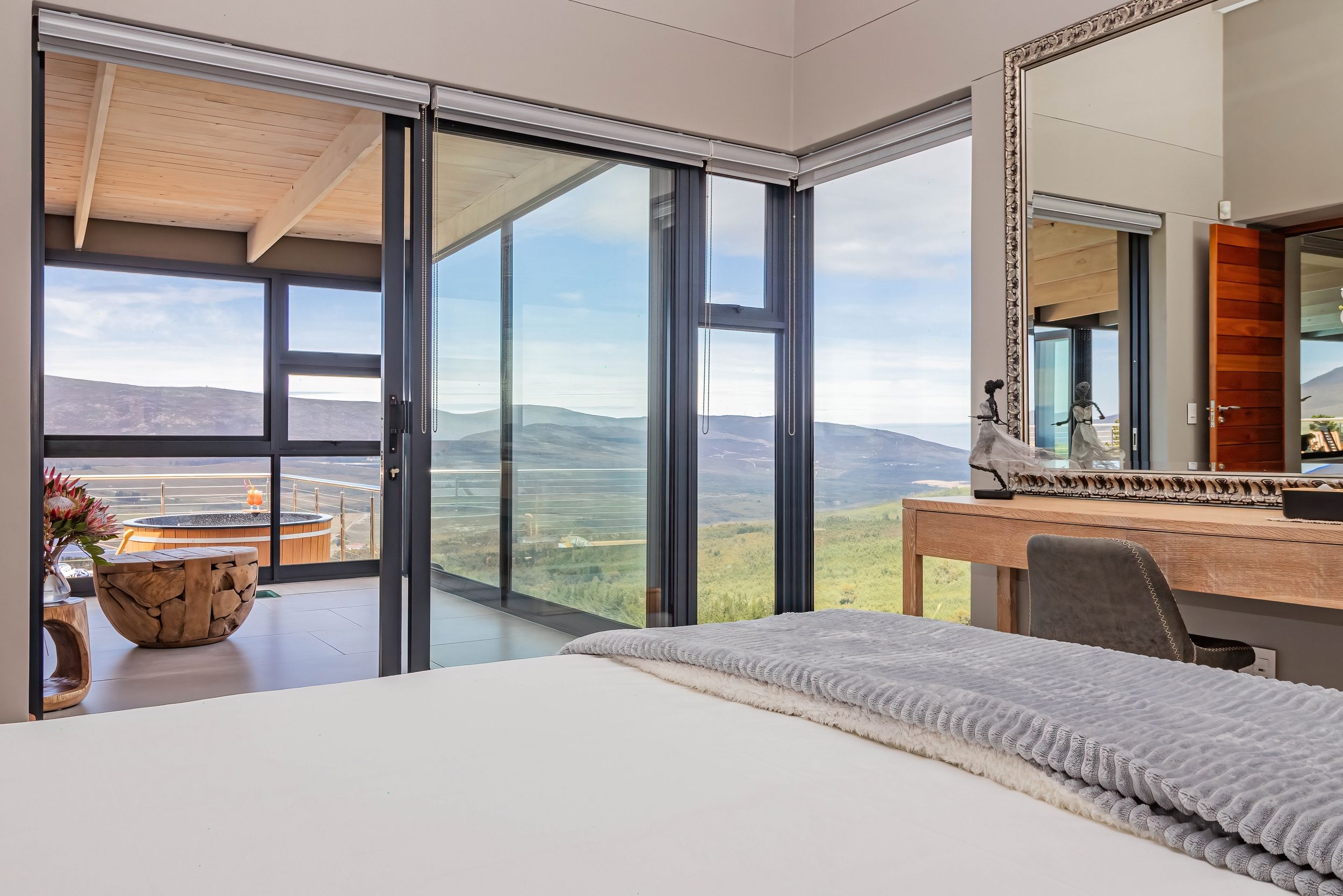 Ein Schlafzimmer mit einem großen Bett, einem Schreibtisch und Blick auf die Berge durch raumhohe Fenster.