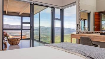 Ein Schlafzimmer mit einem großen Bett, einem Schreibtisch und Blick auf die Berge durch raumhohe Fenster.