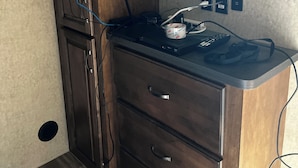 Um canto de um quarto com um armário de madeira, uma mesinha com um controle remoto e uma tomada na parede.