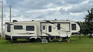 Uma grande motorhome com porta deslizante, pequena varanda e toldo lateral.