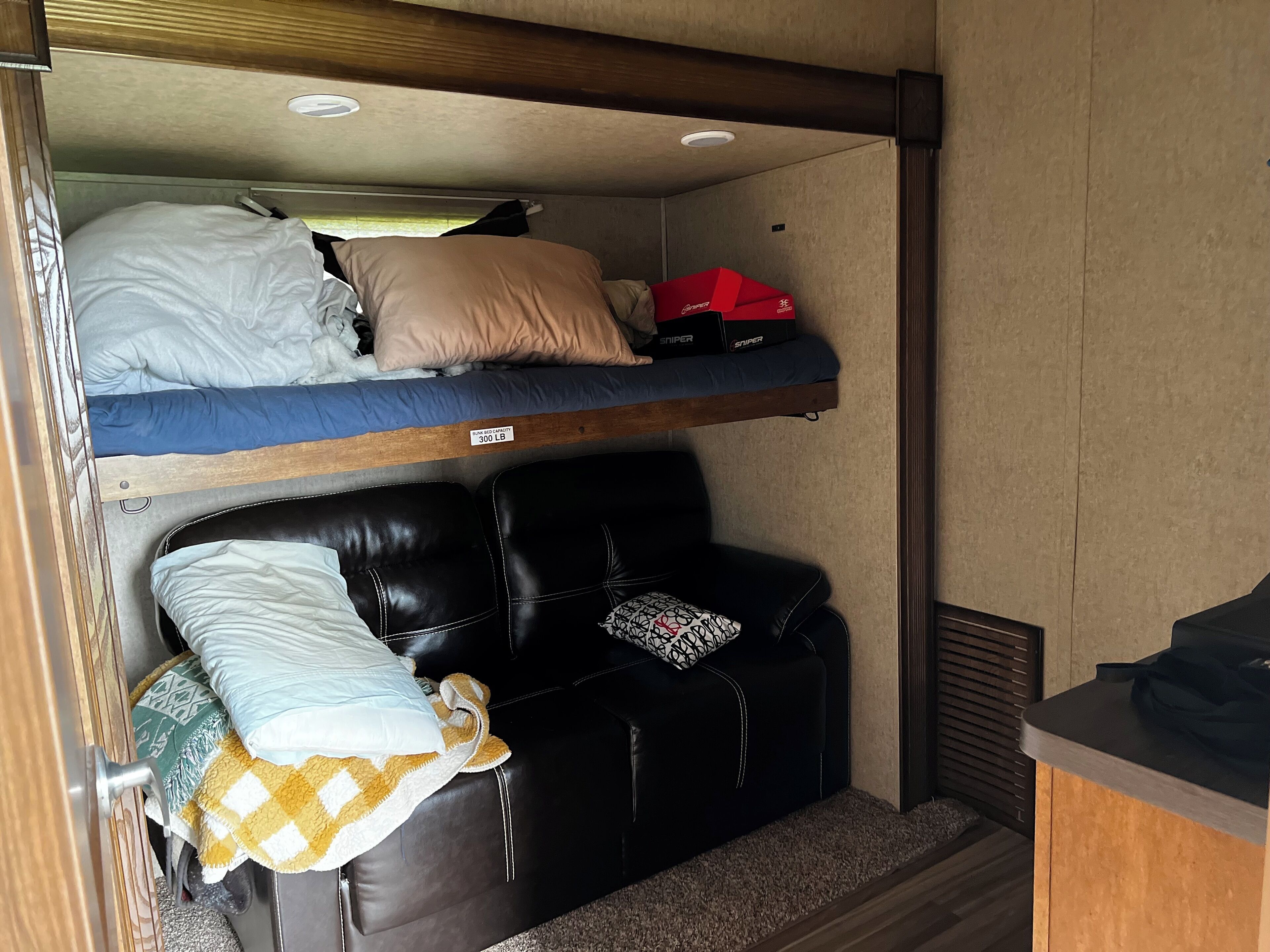 A bunk bed with a label indicating a weight capacity of 300 lb, a black leather couch with a patterned pillow, and a small table with a black surface.