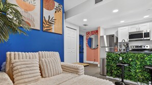 Un salon moderne avec un canapé moelleux, une cuisine équipée d’appareils électroménagers en acier inoxydable et un mur d’accent d’un bleu vif.