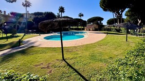 A swimming pool surrounded by a well-maintained lawn, with a clear blue sky and a few trees in the background. - ✨ Luminous townhouse overlooking the Golf on the beach of Novo Sancti Petri (Chiclana de la Frontera)